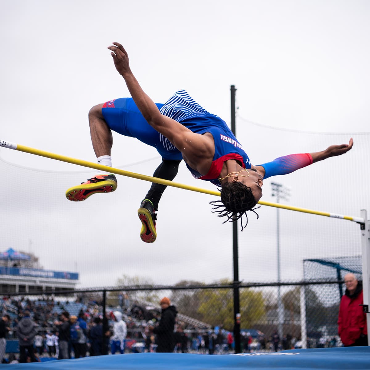 UMass Lowell athlete mid-air during a high jump at a track and field event.