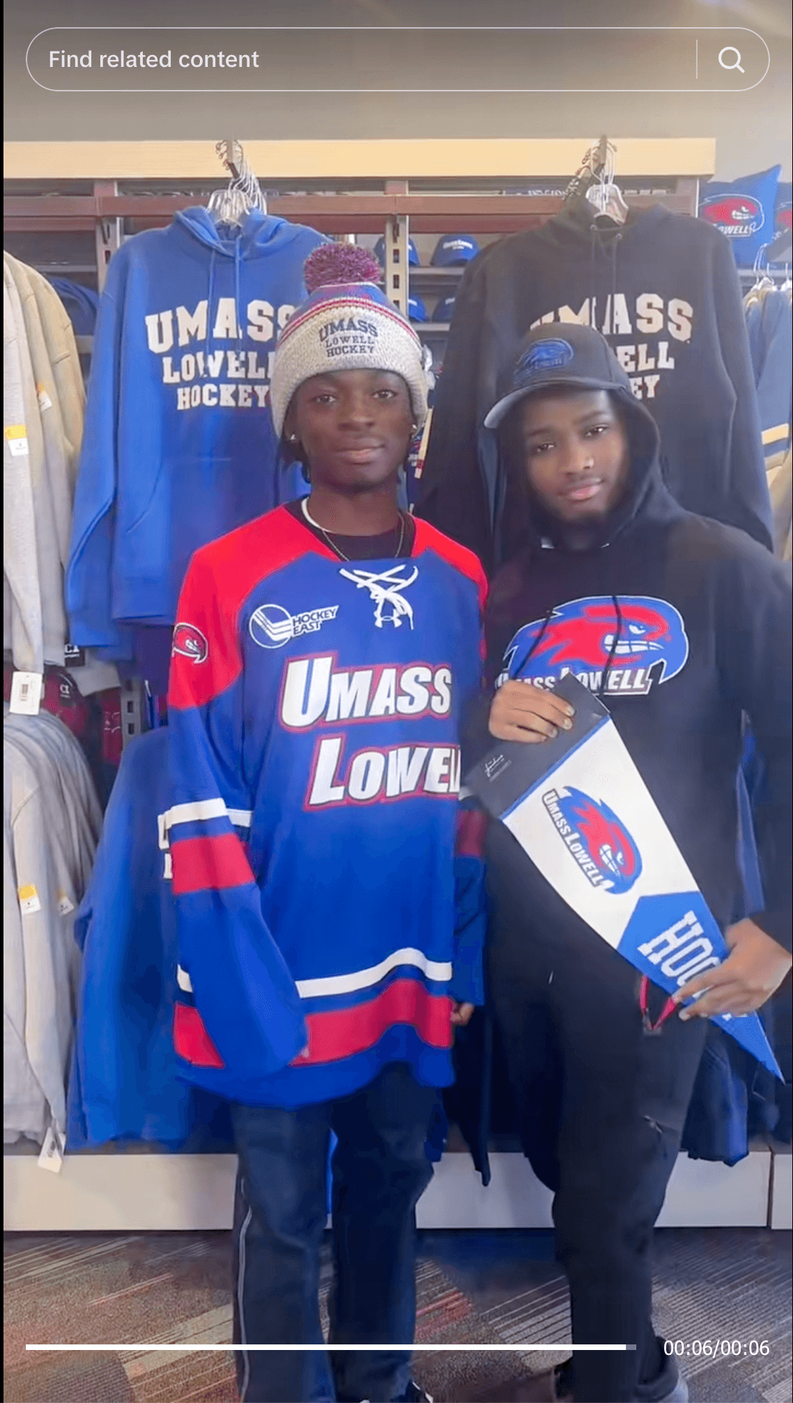 Two students posing in UMass Lowell Hockey gear inside a campus bookstore.